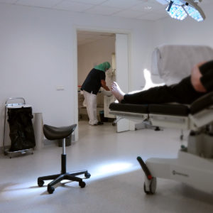 patient ligger på operationsbord, läkare i skyddsmundering tvättar händerna i ett rum utanför